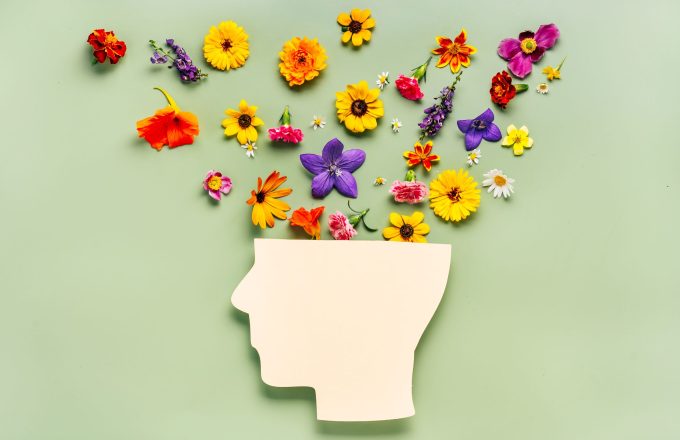 Paper face over pale green background, fresh flowers laid out over top of head representing mental health