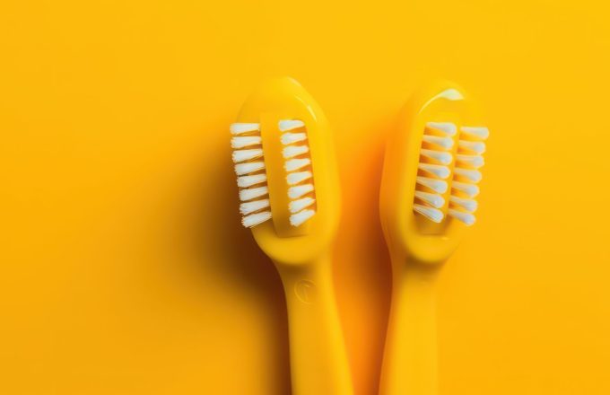 Modern yellow kids toothbrushes on a yellow background. Generative AI.