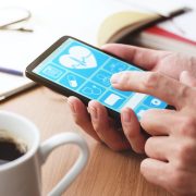 Online healthcare app on smartphone screen. Closeup of male hands touching smartphone screen at table.