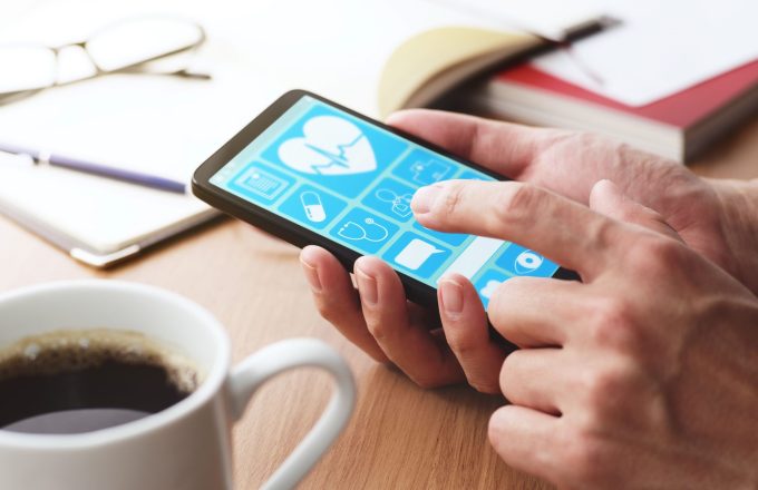 Online healthcare app on smartphone screen. Closeup of male hands touching smartphone screen at table.