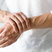 An adult person wearing a white t-shirt holding a painful wrist
