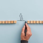 Male hand drawing a connecting line between two sets of wooden blocks fo a silhouetted man to walk across. Conceptual image of teamwork, innovation and knowledge mobilisation.