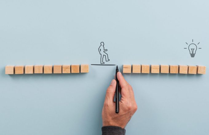 Male hand drawing a connecting line between two sets of wooden blocks fo a silhouetted man to walk across. Conceptual image of teamwork, innovation and knowledge mobilisation.