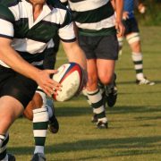 Close-up (legs/torso only), men playing rugby on a grass pitch. Non-professional.