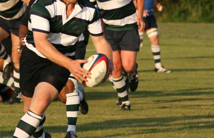 Close-up (legs/torso only), men playing rugby on a grass pitch. Non-professional.
