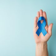 First person top view photo of male hand holding blue silk ribbon in palm symbol of prostate cancer awareness on isolated pastel blue background with blank space