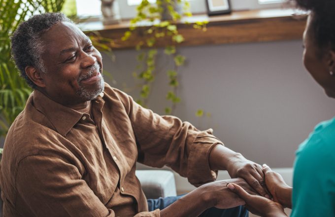 Female healthcare worker holding hands of senior man at care home, focus on hands. Doctor helping old patient with Alzheimer's disease. Female carer holding hands of senior man