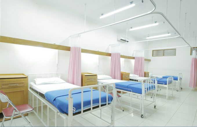 A row of three hospital beds with blue blankets and pink curtains separating each bed.