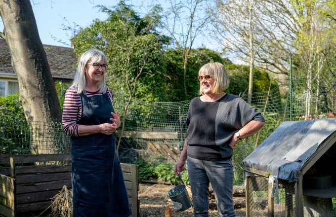 Two women stand chatting in a community garden