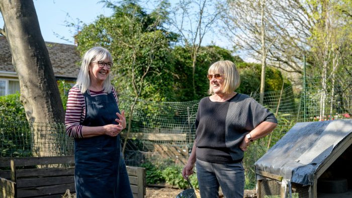 Two women stand chatting in a community garden